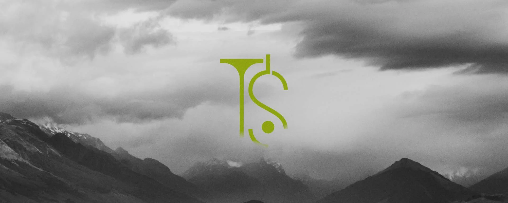 The TS monogram over a dramatic, mist-covered mountain landscape
